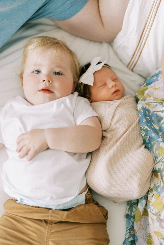 toddler and little newborn sister laying on bed